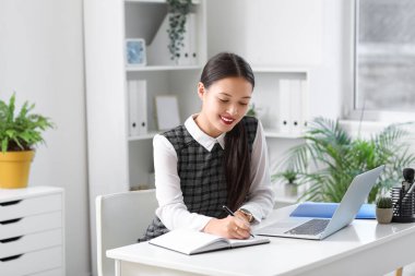 Masasında defterle çalışan Asyalı genç bir iş kadını.