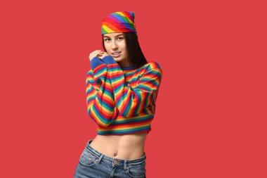 Kırmızı arka planda piercingli, gökkuşağı süveterli güzel bir kadın.