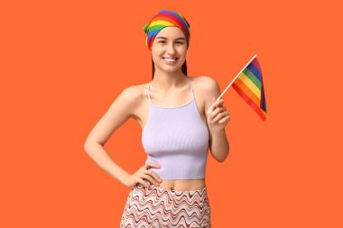 Göbeğinde piercing ve turuncu arka planda LGBT bayrağı olan güzel, mutlu bir kadın.