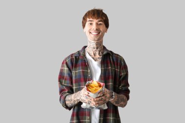 Açık arkaplanda patates cipsi olan dövmeli genç bir adam.