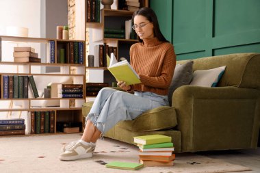 Evdeki kanepede kitap okuyan genç bir kadın.