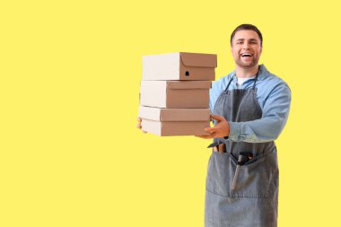 Sarı arka planda ayakkabı kutuları olan erkek ayakkabıcı.