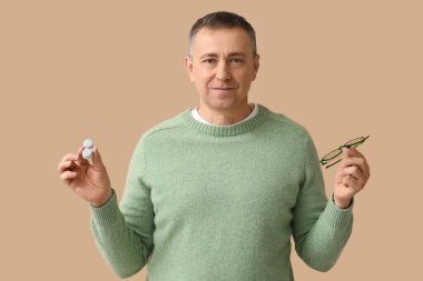 Lens kutusu ve kahverengi arka planda gözlüğü olan olgun bir adam.