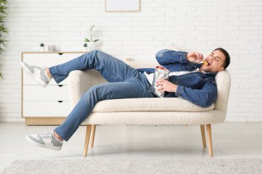 Evde kanepeye uzanmış patates cipsli yakışıklı genç adam.