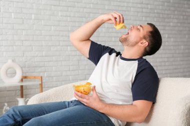 Evde bir kase lezzetli patates cipsiyle yakışıklı bir genç.