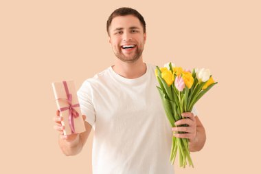 Hediye kutusu ve bej arka planda bir buket güzel lalesi olan yakışıklı genç adam.