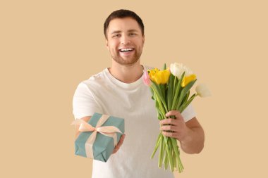 Hediye kutusu ve bej arka planda bir buket güzel lalesi olan yakışıklı genç adam.