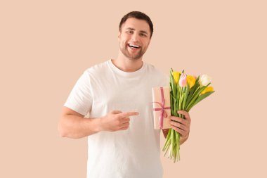 Yakışıklı genç adam hediye kutusunu ve bej arka planda güzel laleleri gösteriyor.