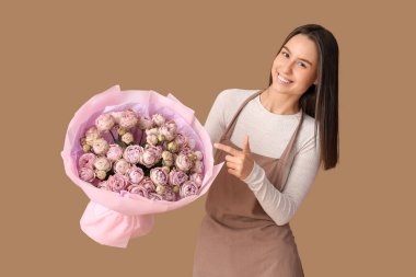 Kahverengi arka planda bir buket güzel gülü gösteren genç teslimatçı kadın.