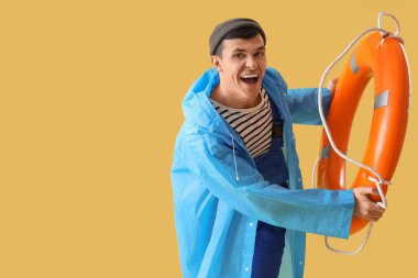 Sarı arka planda halka şamandırası olan yağmurluk giyen genç bir denizci.