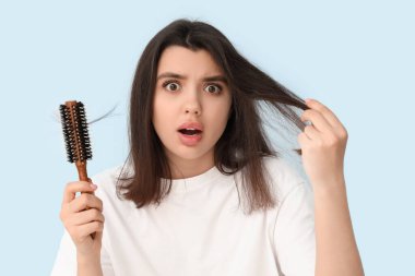 Mavi arka planda saç kaybı sorunu olan stresli genç bir kadın.
