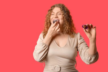 Kırmızı arka planda çikolata şekerlemeleri olan güzel genç bir kadın.