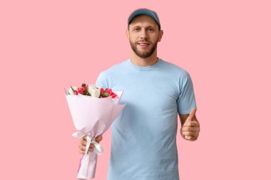 Bir buket güzel lalesi olan genç teslimatçı pembe arka planda baş parmak hareketi gösteriyor.