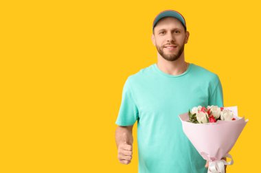 Bir buket güzel lalesi olan genç teslimatçı sarı arka planda baş parmak hareketi gösteriyor.