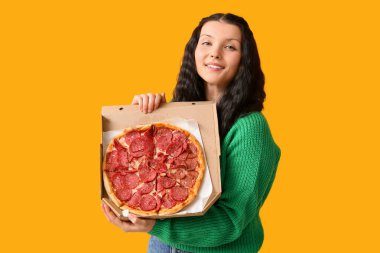 Sarı arka planda lezzetli pizzayla dolu karton bir kutu tutan güzel bir kadın.