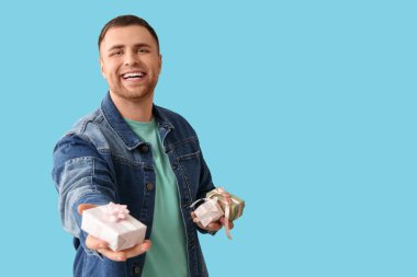 Mavi arka planda hediye kutuları olan yakışıklı genç adam.