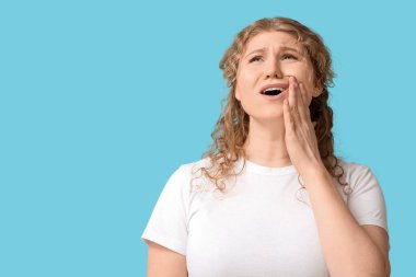 Mavi arka planda diş ağrısından muzdarip güzel genç bir kadın.