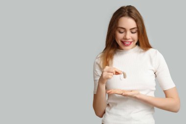 Gri arka planda işitme cihazı olan güzel genç bir kadın.