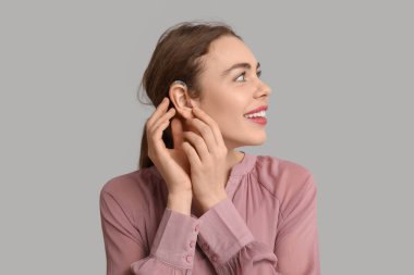 Gri arka planda işitme cihazı olan mutlu genç bir kadın.