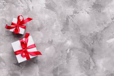 Gri arka planda kırmızı kurdeleyle bağlanmış hediye kutuları. Üst görünüm