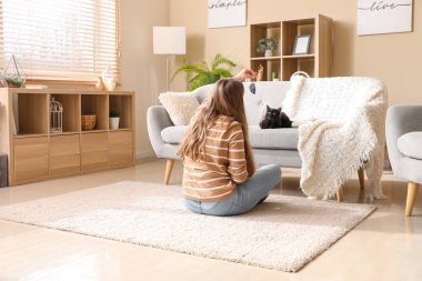 Oturma odasında sevimli siyah kediyle oynayan bir kadın.