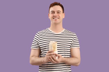 Genç mutlu adam gülümsüyor ve mor arka planda donör kebabı tutuyor.