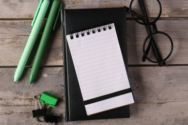 Not defterleri, kalemler, cilt klipleri ve tahta arka plandaki gözlükler