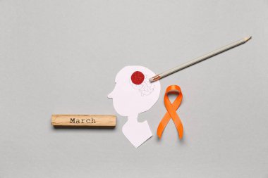 Kağıt insan kafası, kurşun kalem, Kelime Marşı ve gri arka planda turuncu kurdele. Çoklu Skleroz Farkındalık Ayı