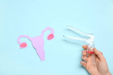 Kağıt uterusu olan kadın eli ve mavi arka planda jinekolojik spekulum.