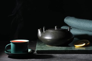 Çaydanlıklı mermer tahta, limon dilimleri ve siyah duvarın yanındaki siyah masada bir fincan sıcak çay.