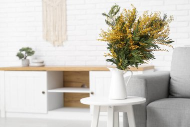 Oturma odasındaki masada güzel mimoza çiçekleri olan vazo.