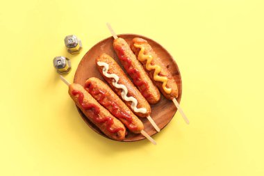 Sarı arka planda farklı soslu lezzetli mısırlı sosis tabağı.