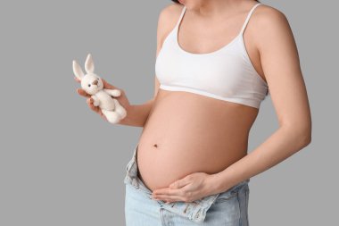 Aydınlık arka planda oyuncak tavşanı olan genç hamile kadın, yakın plan.