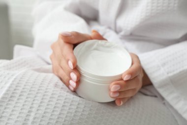 Bornozlu kadın elinde krema kavanozu, yakın plan.