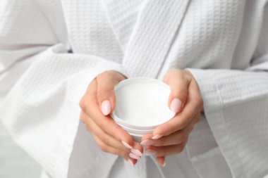 Bornozlu kadın elinde krema kavanozu, yakın plan.