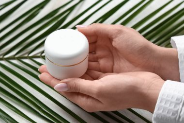 Arka planda krema kavanozu ve palmiye yaprağı olan kadın elleri, yakın plan.