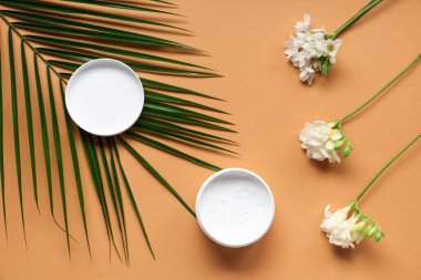 Renkli arkaplanda krema kavanozu, palmiye yaprağı ve frezya çiçekleri ile kompozisyon