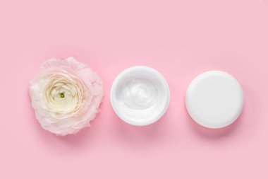 Bir kavanoz krema ve pembe arka planda ranunculus çiçeği.