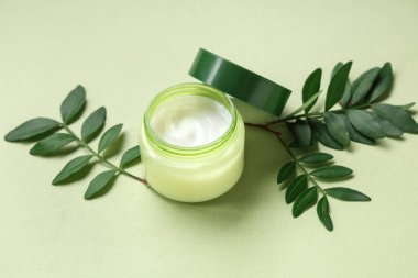 Yeşil arka planda krema ve bitki yapraklarıyla kompozisyon