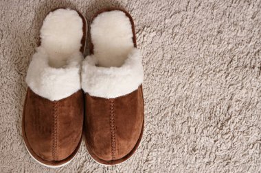 Yumuşak kahverengi terlikler halıda, yakın plan.