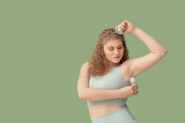 Yeşil arka plana deodorant süren güzel genç bir kadın.