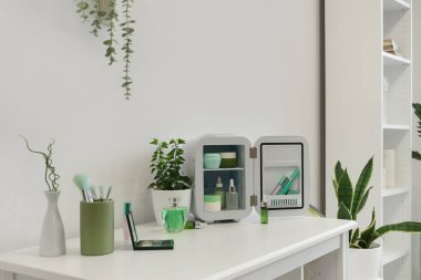 Ürünleri, çiçekleri ve ışık duvarının yanındaki masada fırçaları olan kozmetik buzdolabını aç