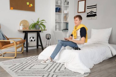 Erkek öğrenci yatak odasında dizüstü bilgisayar kullanıyor.