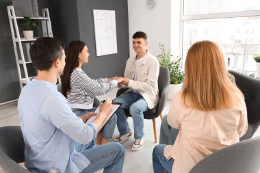 Male psychologist writing in clipboard at group therapy session