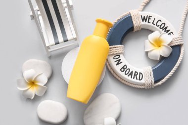 Beyaz arka planda bir şişe güneş kremi, can simidi yüzüğü ve şezlong.