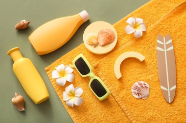 Yeşil arka planda güneş kremi, güneş gözlüğü ve havlu şişeleri