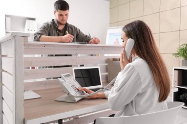 Kadın resepsiyonist hastanede telefonla konuşuyor.