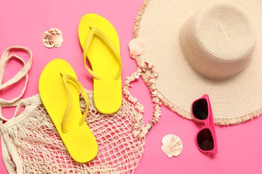 İpli çanta, hasır şapka, güneş gözlüğü ve pembe arka planda deniz kabukları.