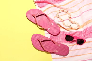 Sarı arka planda deniz kabuğu kolyesi, güneş gözlüğü ve battaniyeli terlikler.