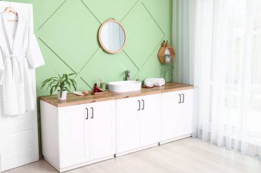 Katlanan ekran, küvetli çekmeceler ve banyoda yeşil duvarın yanında banyo malzemeleri.